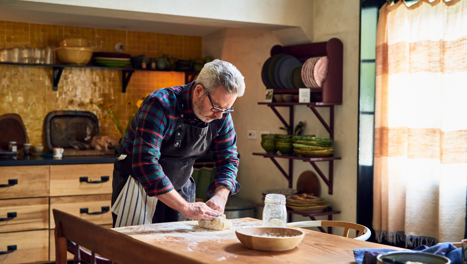 Mann knetet Sauerteig auf einem bemehlten Holztisch in der Küche.