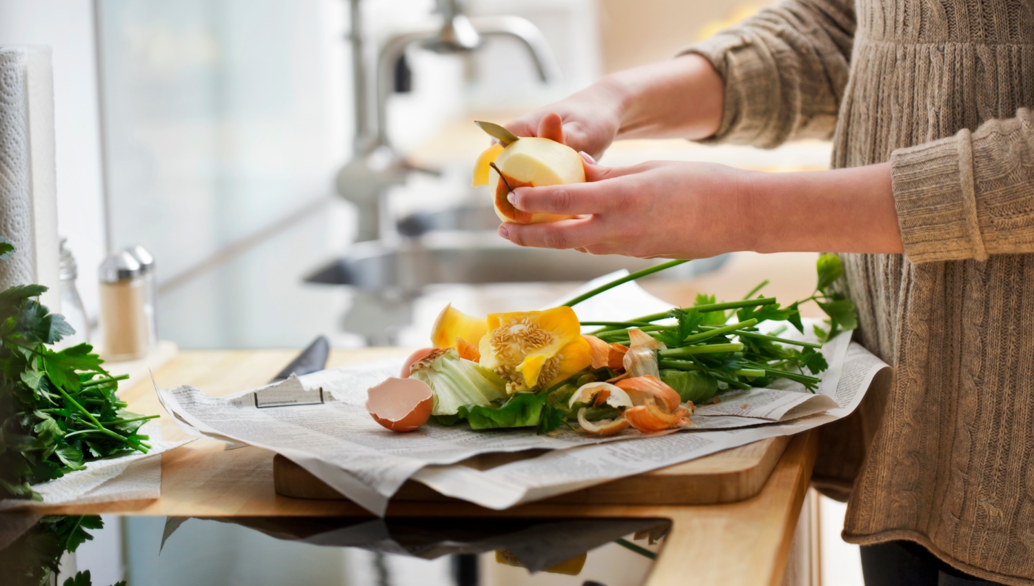 Person schält Apfel in moderner Küche, weitere Gemüsereste auf der Arbeitsplatte.