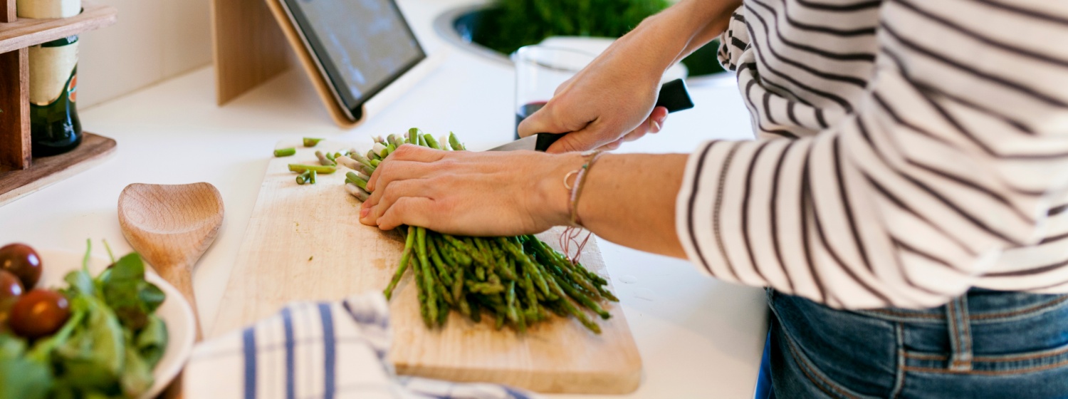 Person schneidet frischen grünen Spargel auf einem Holzbrett.