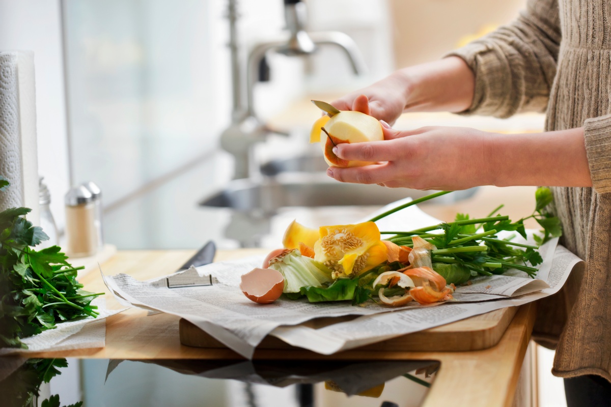 Person schält Apfel in moderner Küche, weitere Gemüsereste auf der Arbeitsplatte.