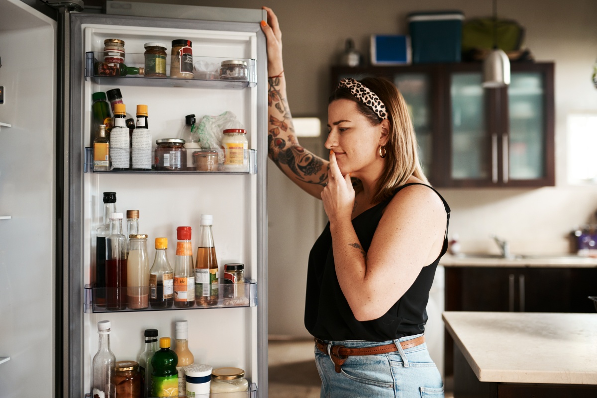 Eine Frau schaut in den offenen Kühlschrank, der mit verschiedenen Lebensmitteln gefüllt ist.