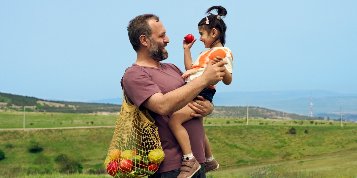 Landwirt steht auf der Weide und hält seine Tochter in den Armen.