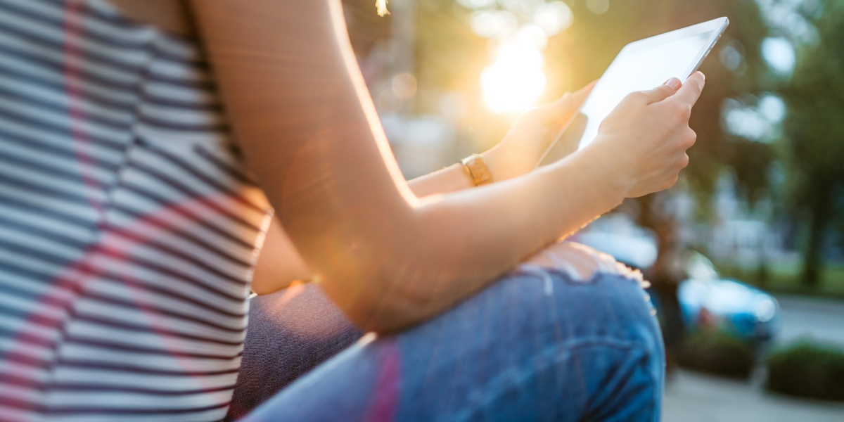 Person sitzt im Freien und benutzt ein Tablet bei Sonnenlicht.