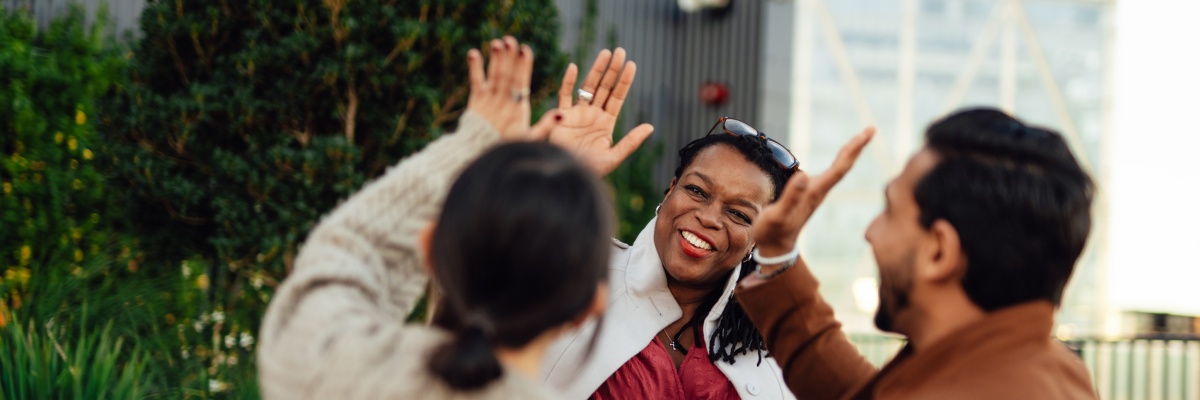 Fröhliche Frau klatscht in die Hände zweier Personen, städtischer Hintergrund.