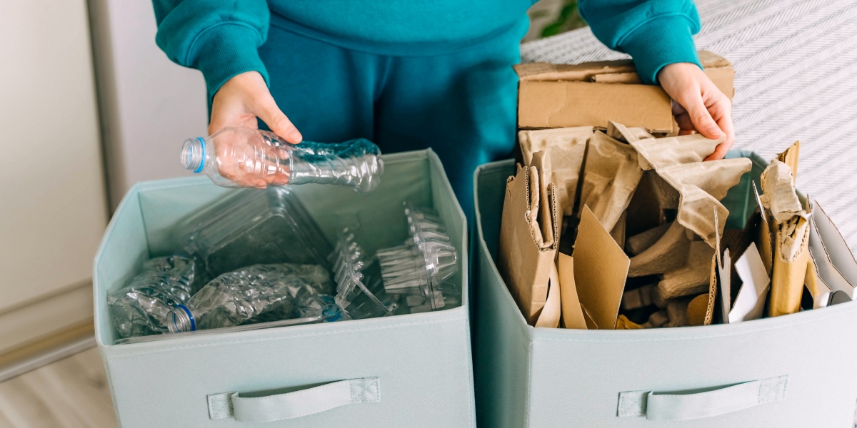 Person sortiert PET-Flaschen und Papiermüll.