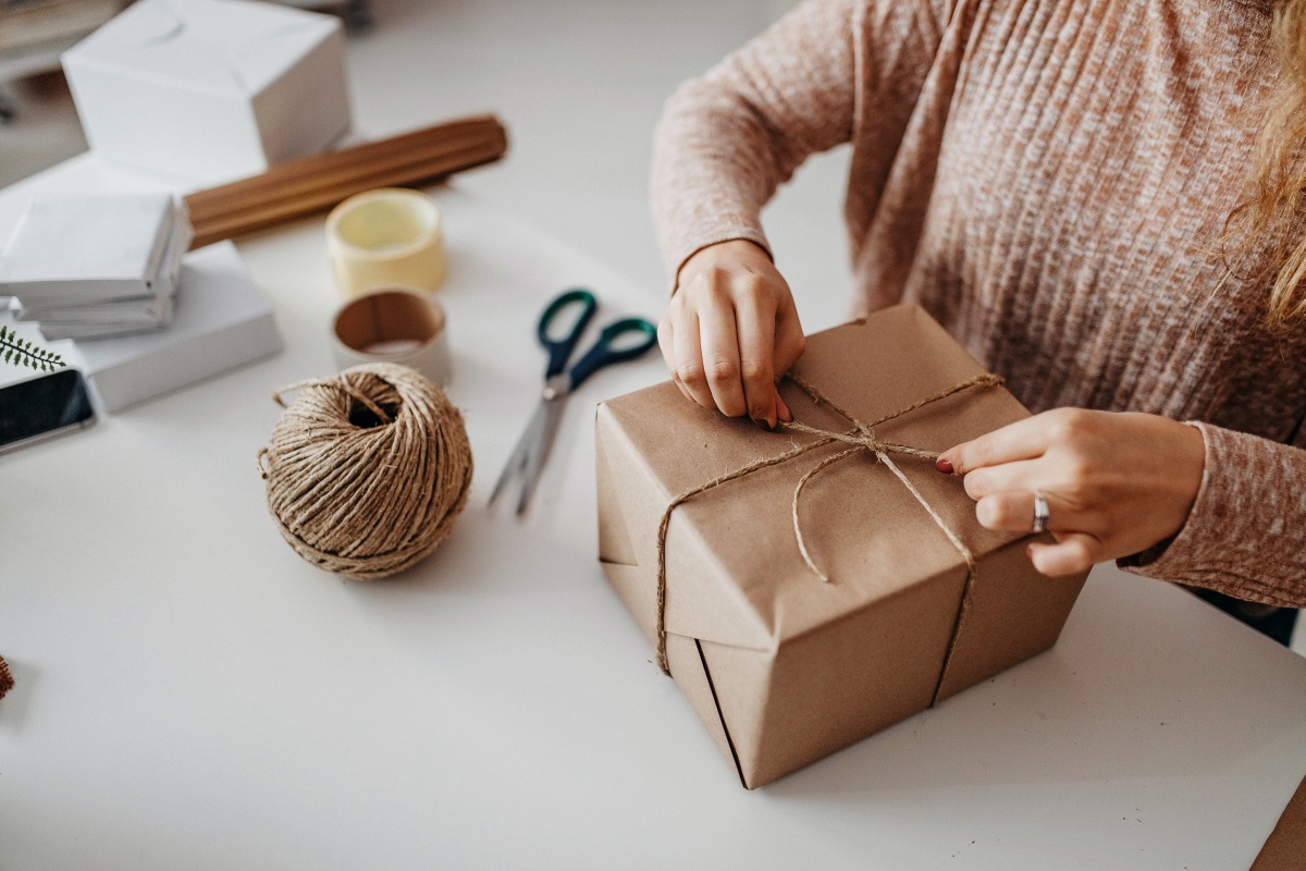 Frau verpackt Geschenk in braunem Papier mit Juteschnur, umgeben von Verpackungsmaterialien.