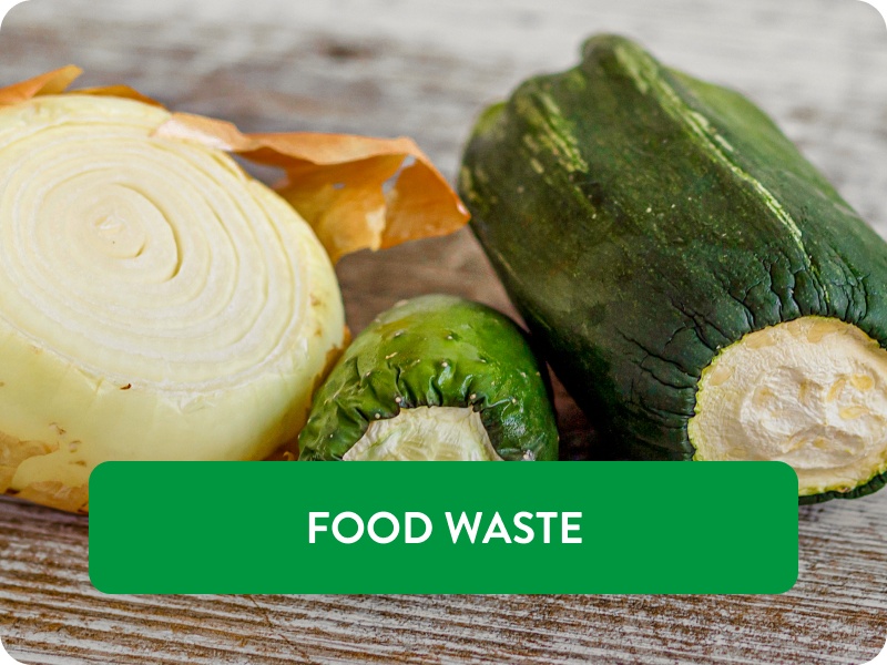 Eine ältere, angeschnittene Zwiebel, Zucchini und Gurke liegen nebeneinander auf einer Küchenplatte.