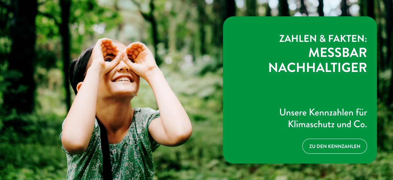 Ein Kind hält seine Hände wie ein Fernglas vor die Augen und betrachtet die Bäume im Wald.