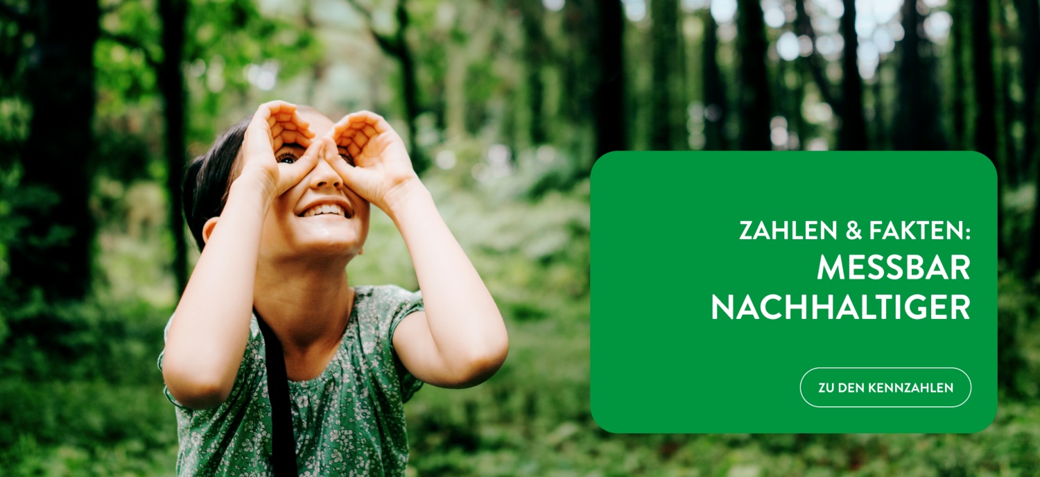 Ein Kind hält seine Hände wie ein Fernglas vor die Augen und betrachtet die Bäume im Wald.