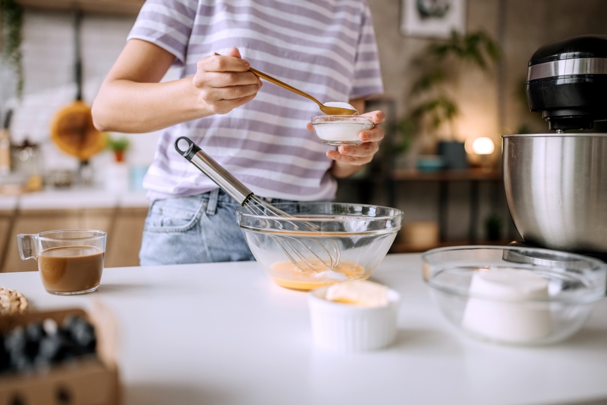 Person fügt Zucker in eine Schüssel mit Eiern, um einen Kuchen zu backen.