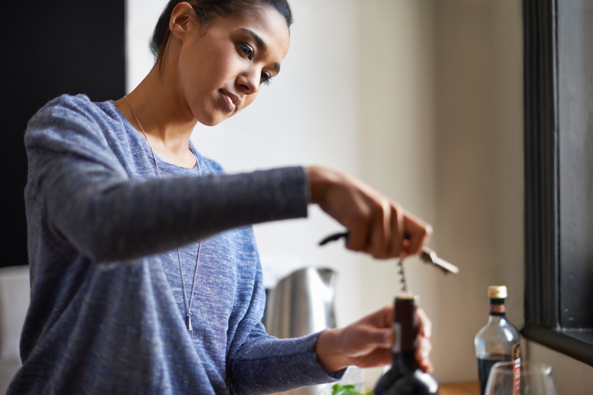 Eine junge Frau löst den Korken einer Flasche Wein mit einem Korkenzieher