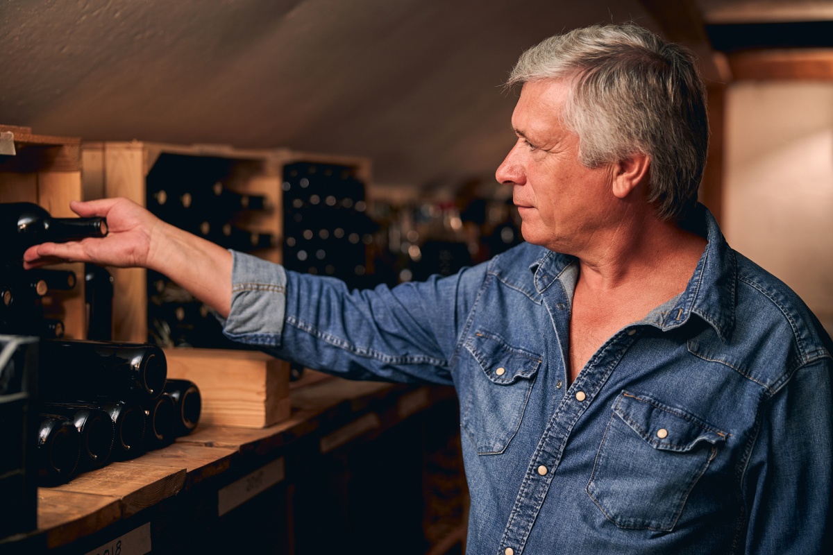 Mann legt eine Weinflasche zum Lagern in ein Weinregal.