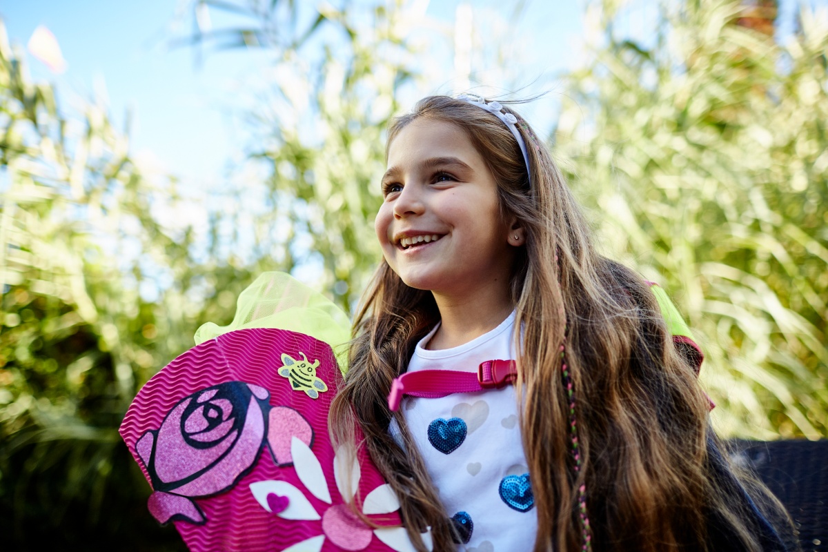 Fröhliches Mädchen mit rosa Schultüte und Schulrucksack im Freien.