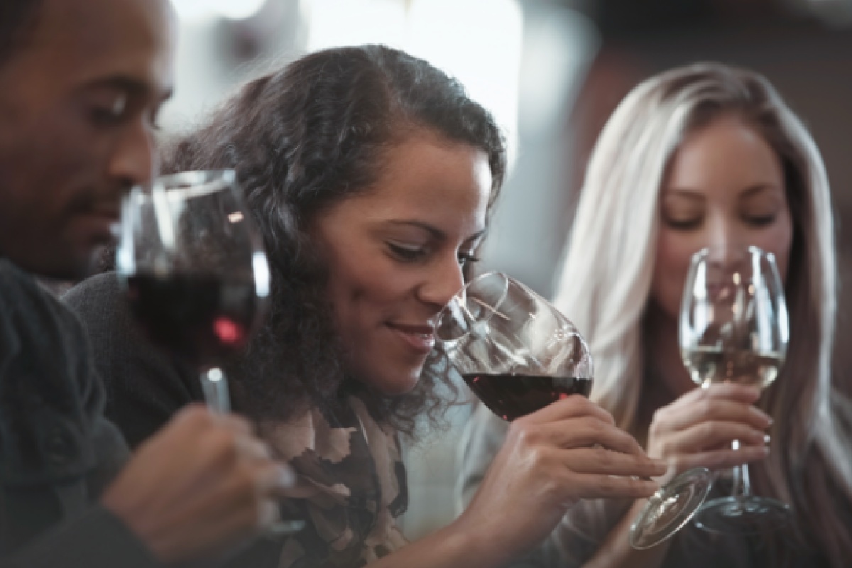 Drei Personen genießen eine Weinprobe, halten Gläser mit Rot- und Weißwein und riechen konzentriert am Wein.