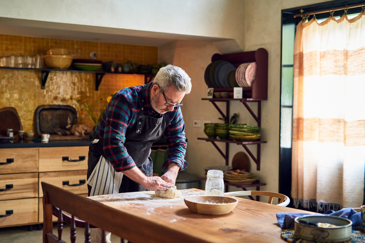 Mann knetet Sauerteig auf einem bemehlten Holztisch in der Küche.