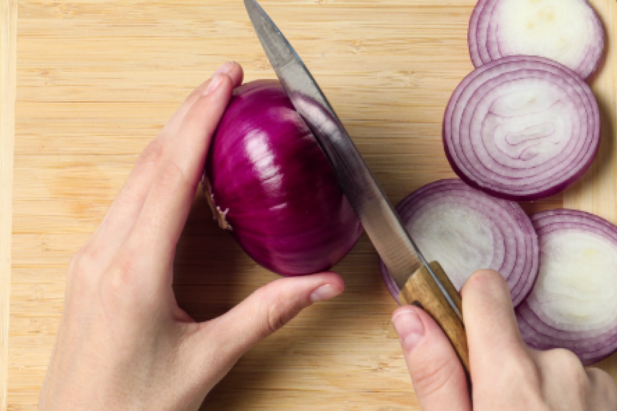 Eine Person schneidet eine rote Zwiebel in Scheiben.