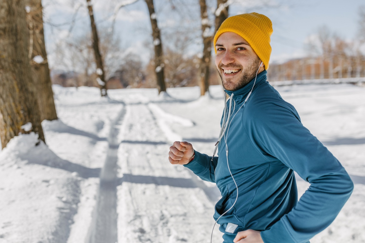 Ein Mann mit Sportkleidung und Mütze joggt auf schneebedeckter Laufstrecke im Winter.