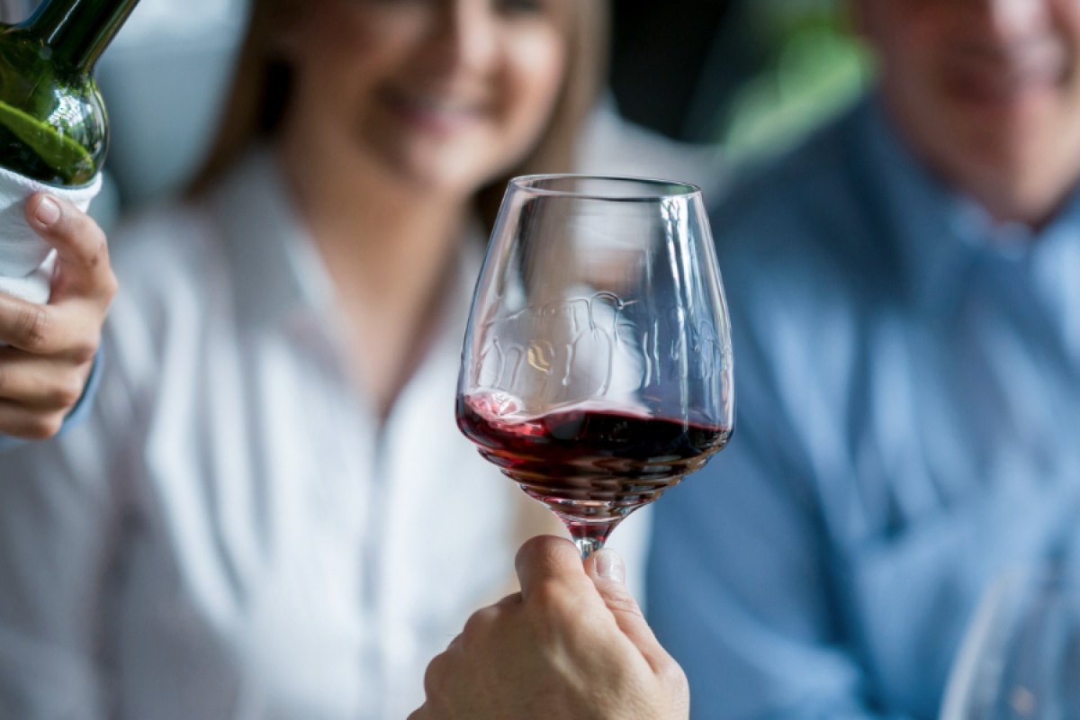 Rotweinglas indem der Maragoni-Effekt eintritt, im Hintergrund Personen und ein Kellner.