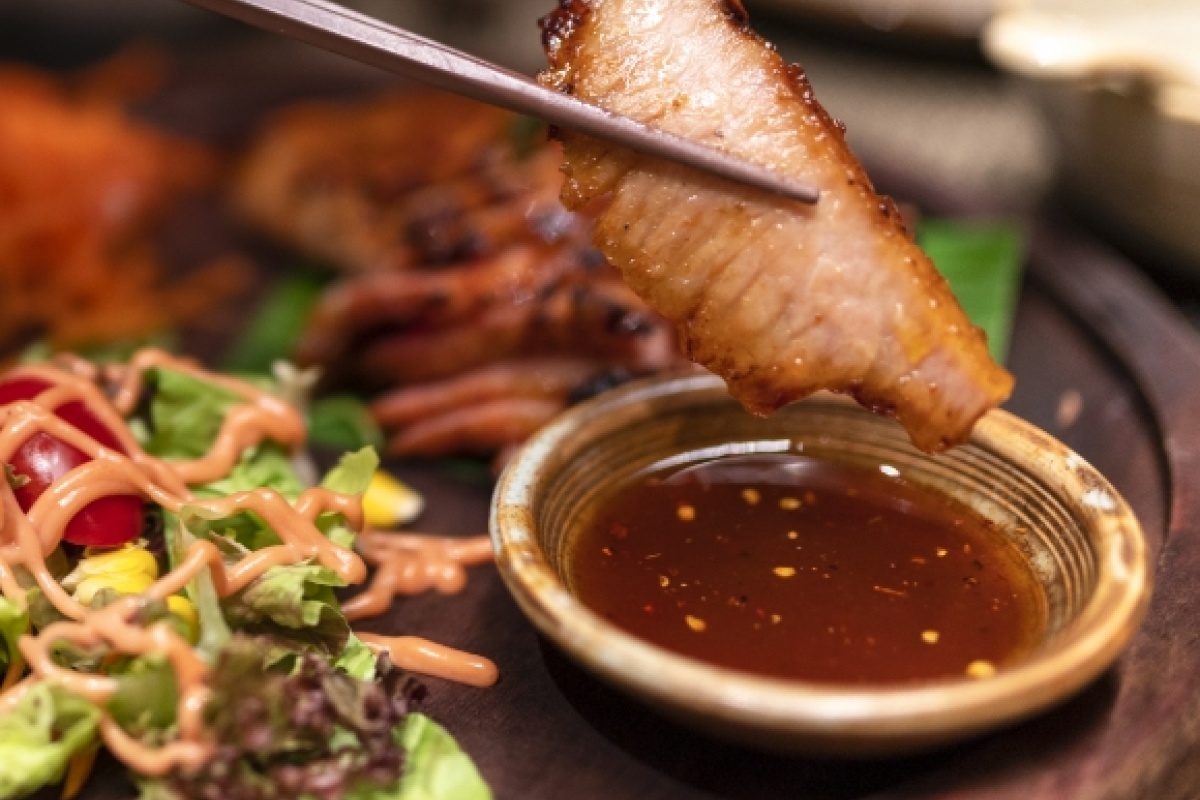 Gegrilltes Fleischstück in Stäbchen über einer Schale mit Soße, daneben frischer Salat mit Dressing, Nahaufnahme.