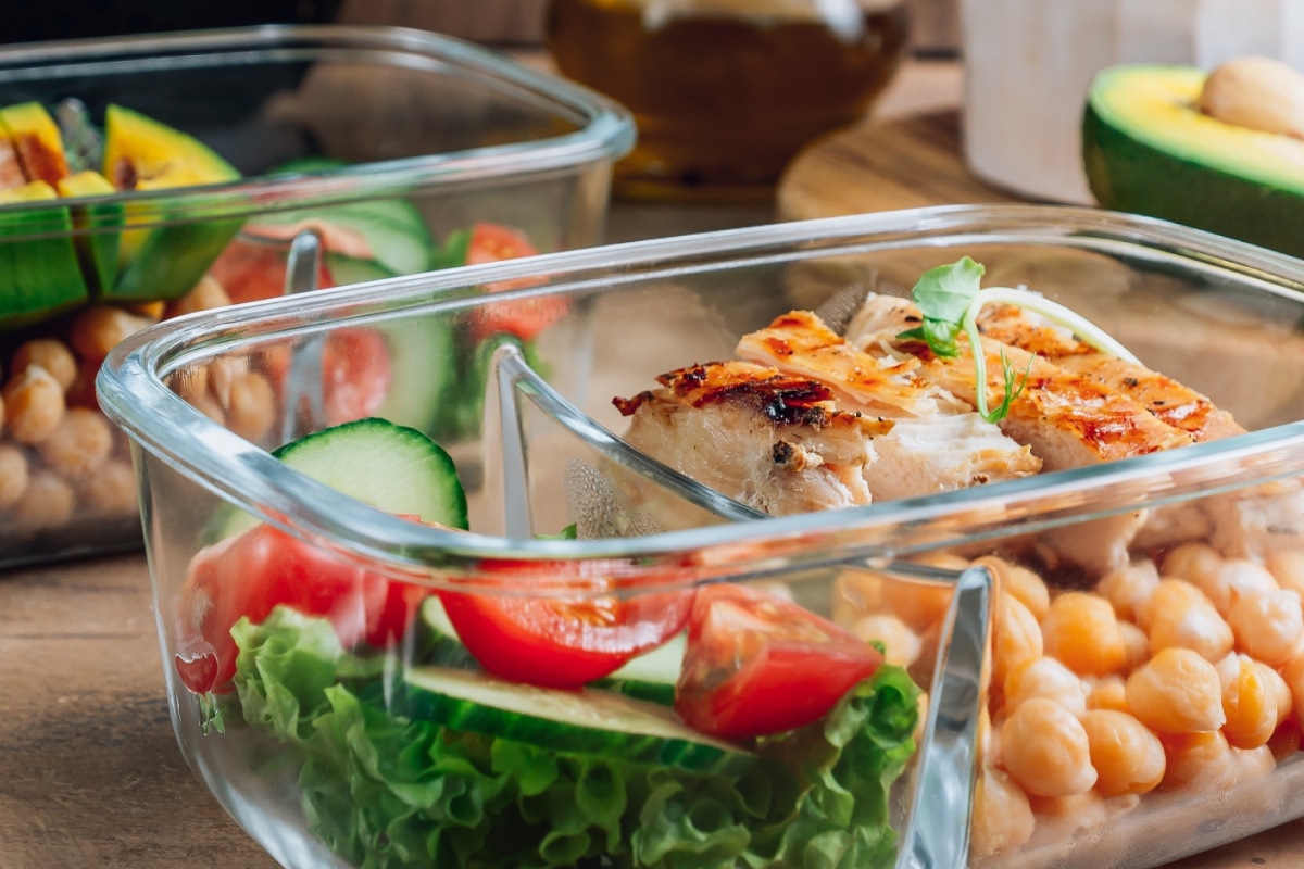 Glasbehälter mit frischem Salat, Kichererbsen und gegrilltem Hähnchen.