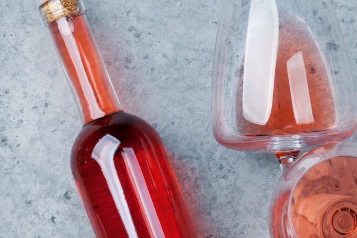 Flasche Roséwein und ein gefülltes Weinglas auf einer grauen Steinoberfläche.