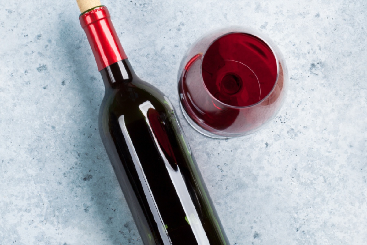 Flasche Rotwein und ein gefülltes Weinglas auf einer grauen Steinoberfläche.