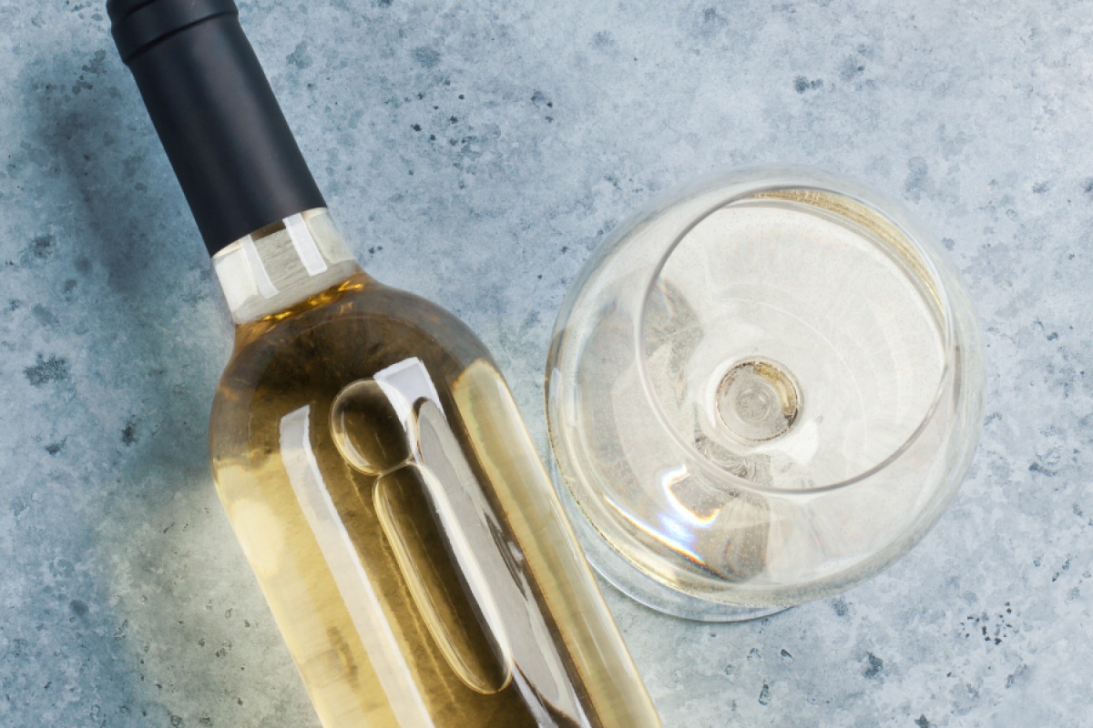 Flasche Weißwein und ein gefülltes Weinglas auf einer grauen Steinoberfläche.