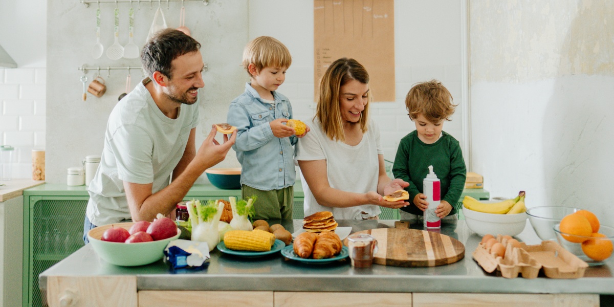 Familie bereitet gemeinsam Frühstück in der Küche zu und lacht.