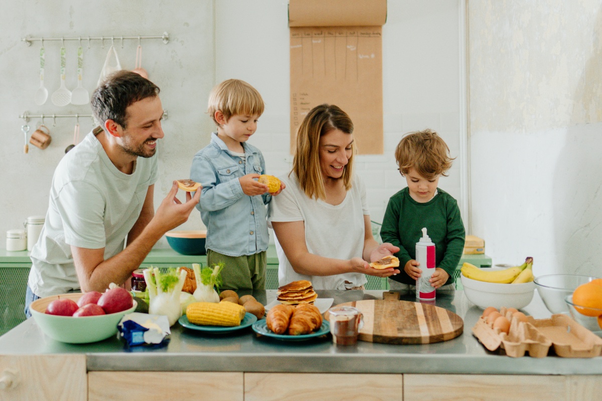 Familie bereitet gemeinsam Frühstück in der Küche zu und lacht.