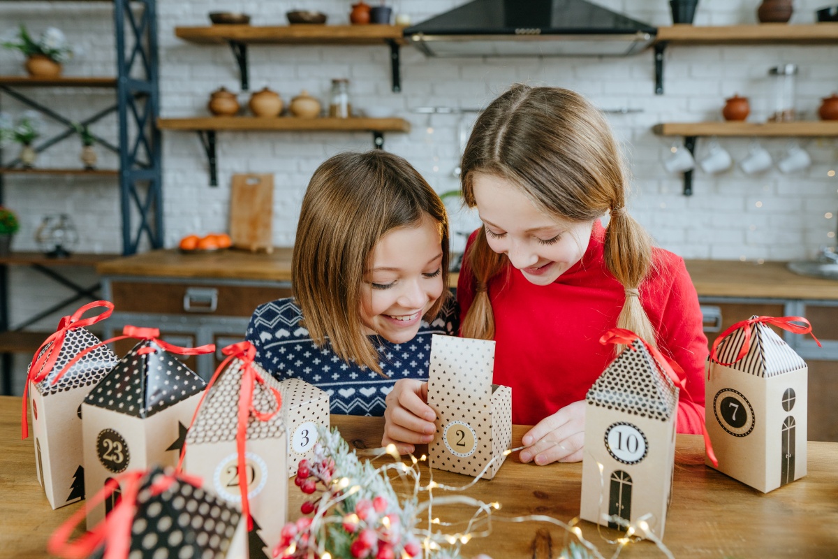 Zwei Mädchen öffnen fröhlich ein Türchen eines selbst befüllten Adventskalender.