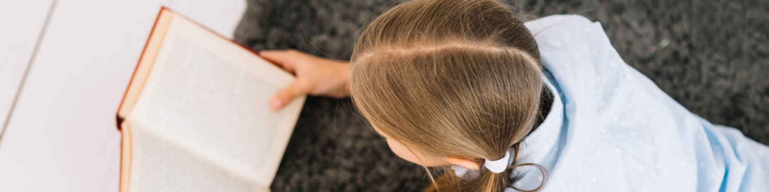 Mädchen liest auf dem Boden liegend ein Buch.
