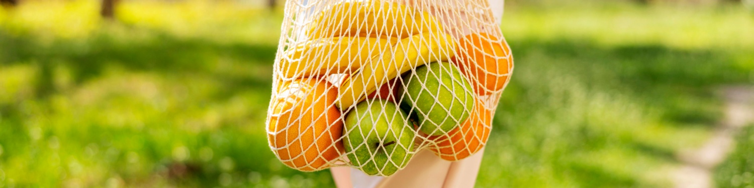 Netzbeutel mit Bananen, Orangen und Äpfeln im Freien.