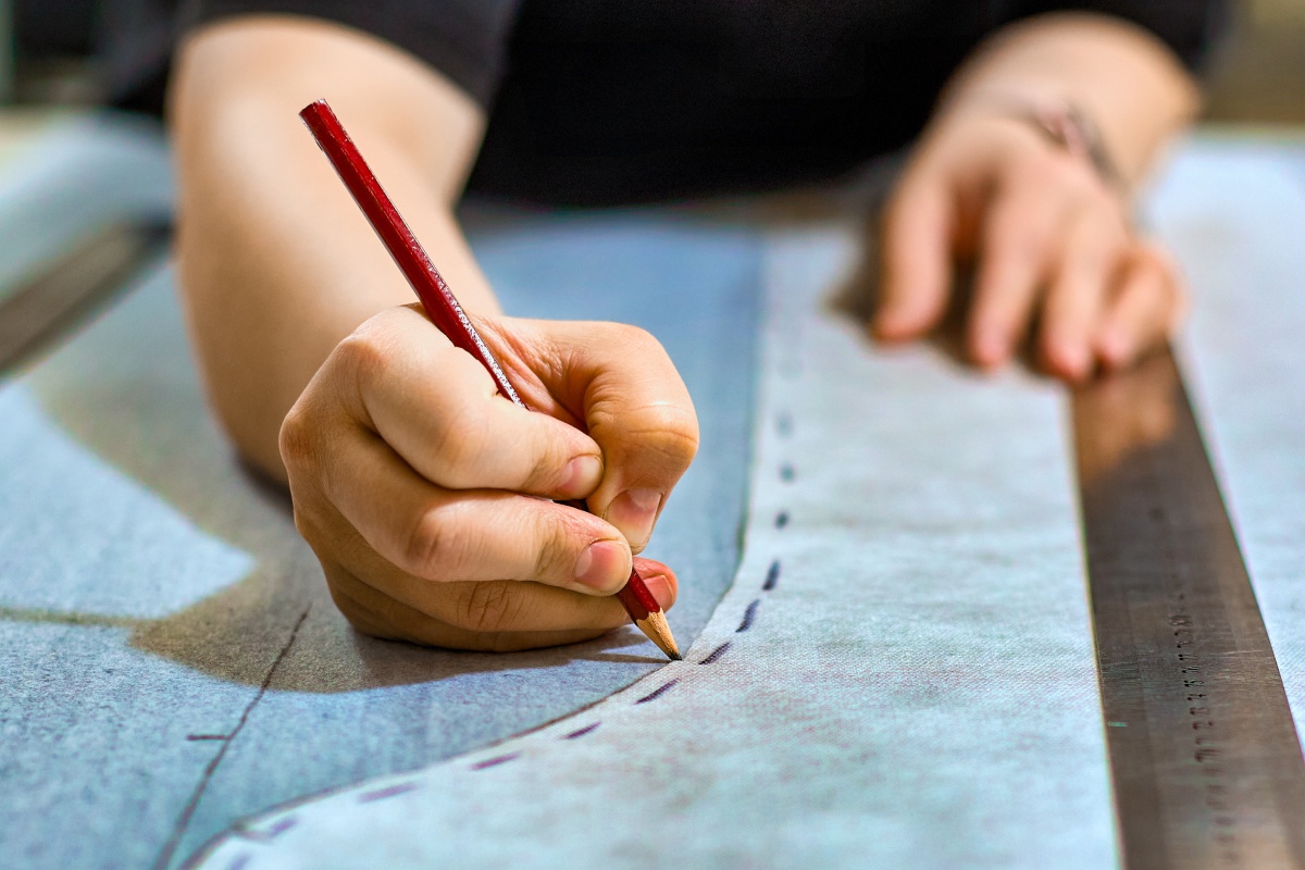 Eine Hand zeichent eine Naht auf einem Stück Stoff auf