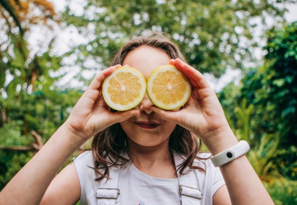 Ein junges Mädchen hält sich zwei Zitronenhälften als Brille vor die Augen