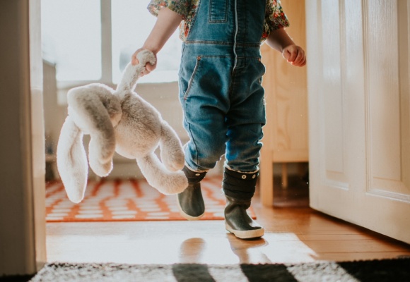 Eine Kleinkind läuft mit seinem Kuscheltier durch das Haus.