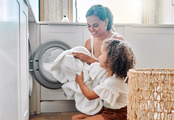 Eine Frau und ein Mädchen räumen gemeinsam weiße Wäsche in die Waschmaschine.