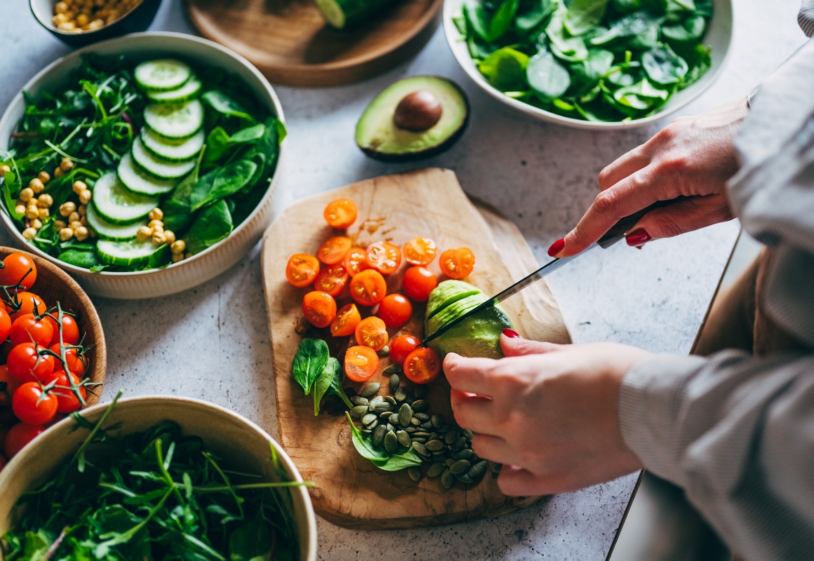 Eine Frau schneidet auf einem Holzbrett Tomaten und Avocado für einen frischen Salat.