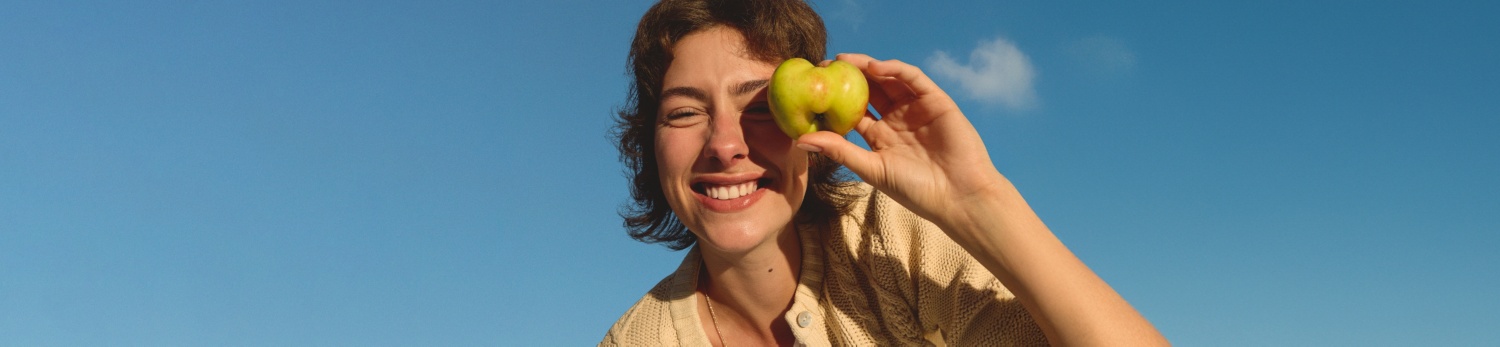 Eine Frau hält einen krummen Apfel vor sich.