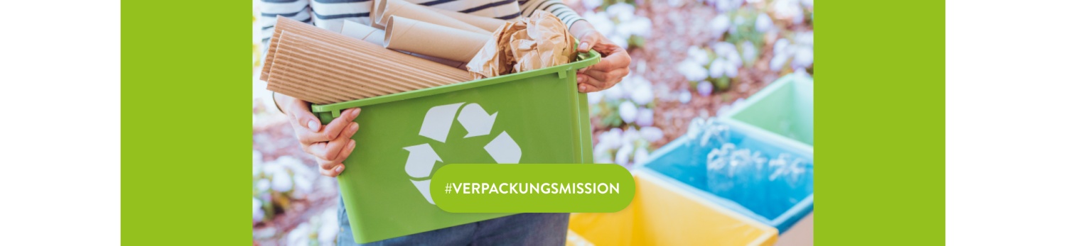 Person trägt Mülleimer mit Papier-Verpackungen, im Hintergrund mehr Behälter zum Mülltrennen für die Kreislaufwirtschaft.