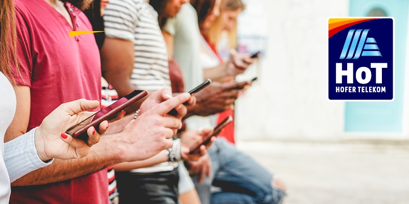 Pet oseb v rokah drži telefon, oblečeni so moderno, delujejo sproščeno, v desnem vogalu pa piktogram za HOFER TELEKOM.