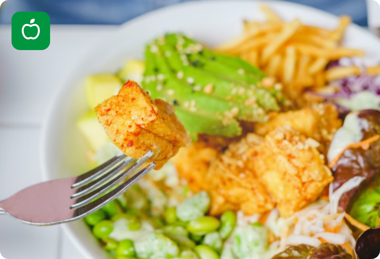 Gabel mit Tofu-Stück über einer farbenfrohen Salatschüssel mit Avocado, Edamame, Pommes und Blattsalat.