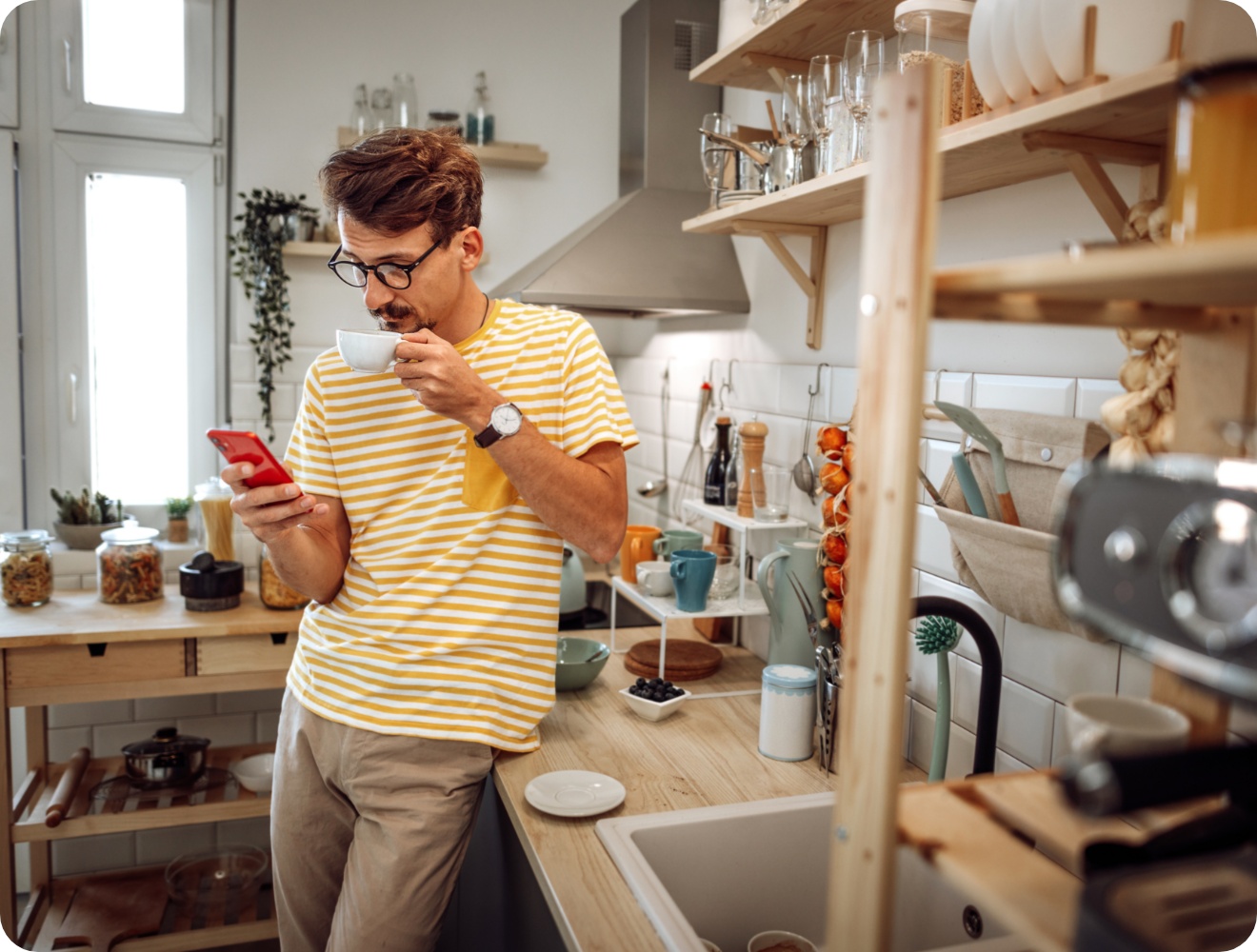Mann in gestreiftem Shirt trinkt eine Tasse Kaffee und schaut in seinem Smartphone nach Sonderangeboten.
