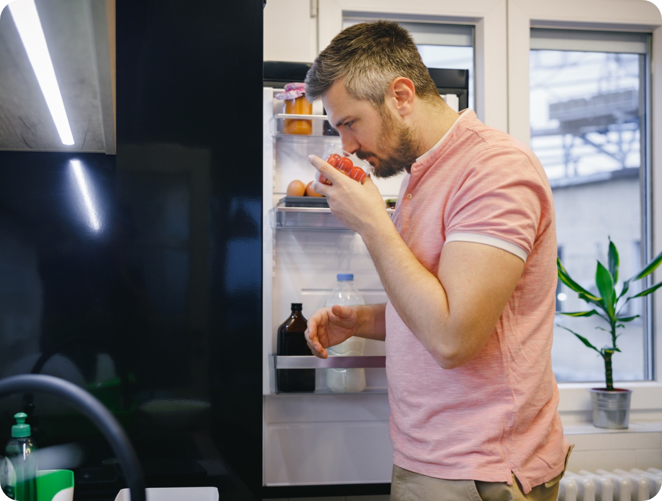 Mann in rosa Polohemd riecht an Tomaten vor offenem Kühlschrank.