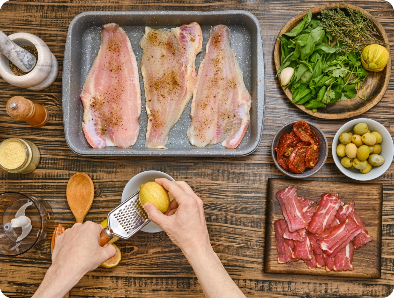 Roh marinierter Fisch in Auflaufform, umgeben von Kräutern, Oliven, getrockneten Tomaten und geriebener Zitrone auf Holztisch.