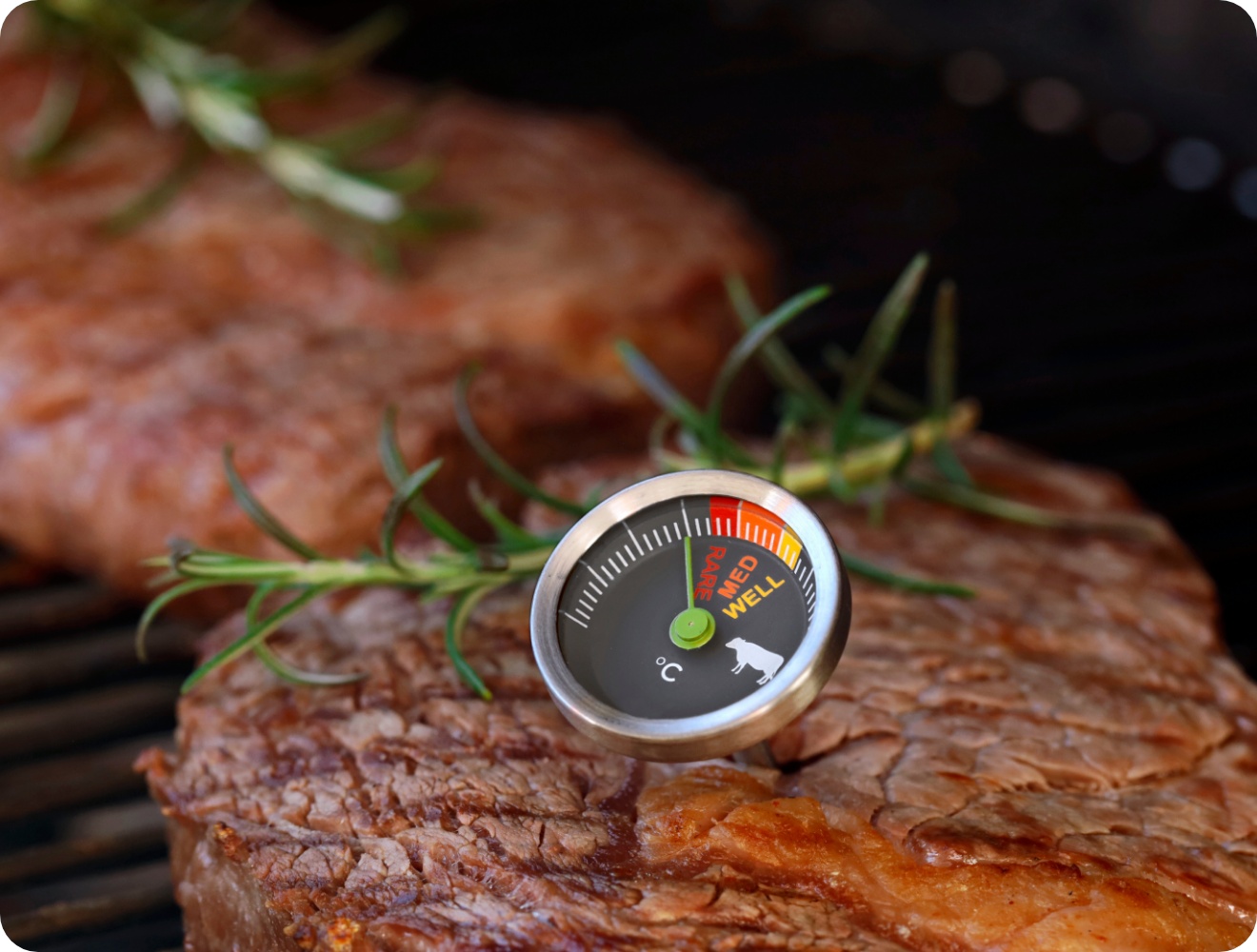 Medium gegrilltes Steak mit Fleischthermometer und Rosmarinzweig auf Grillrost, Temperaturanzeige gut sichtbar.