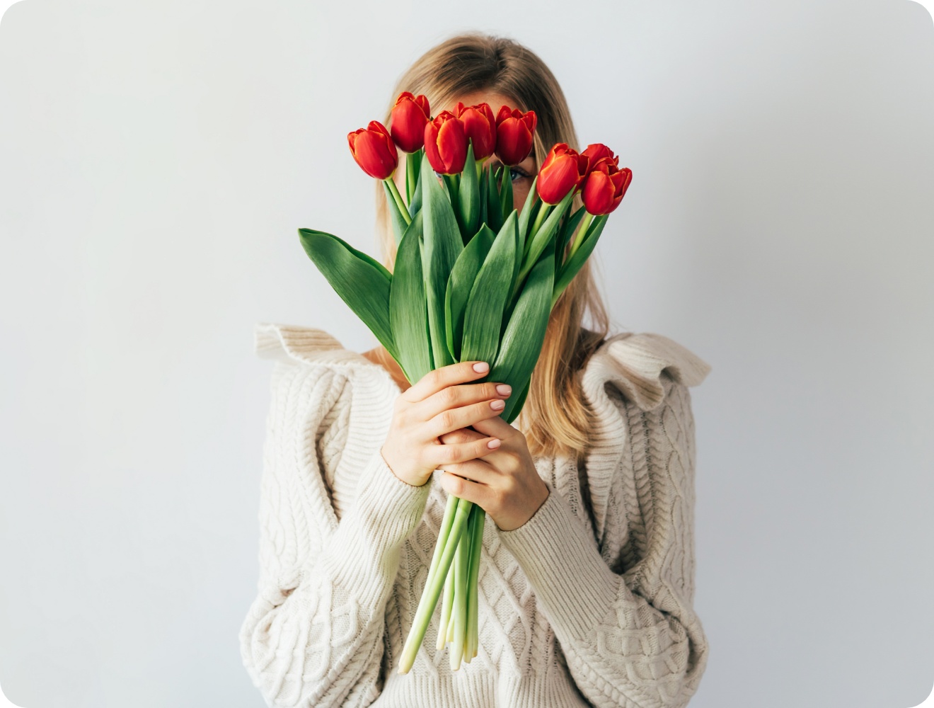 Eine Frau hält sich einen Strauß mit roten Tulpen vor ihr Gesicht.
