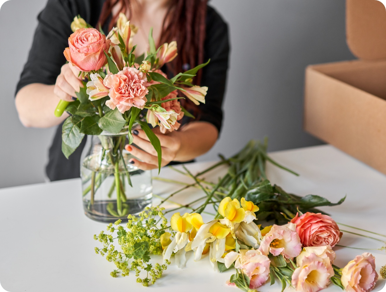 Frau steckt Frühlingsblumen in dern Farben gelb, oragen und rosa in eine durchsichtige Vase.