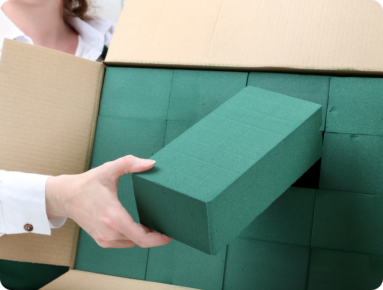 Person holt einen grünen Steckschaumblock aus einer Pappkiste.
