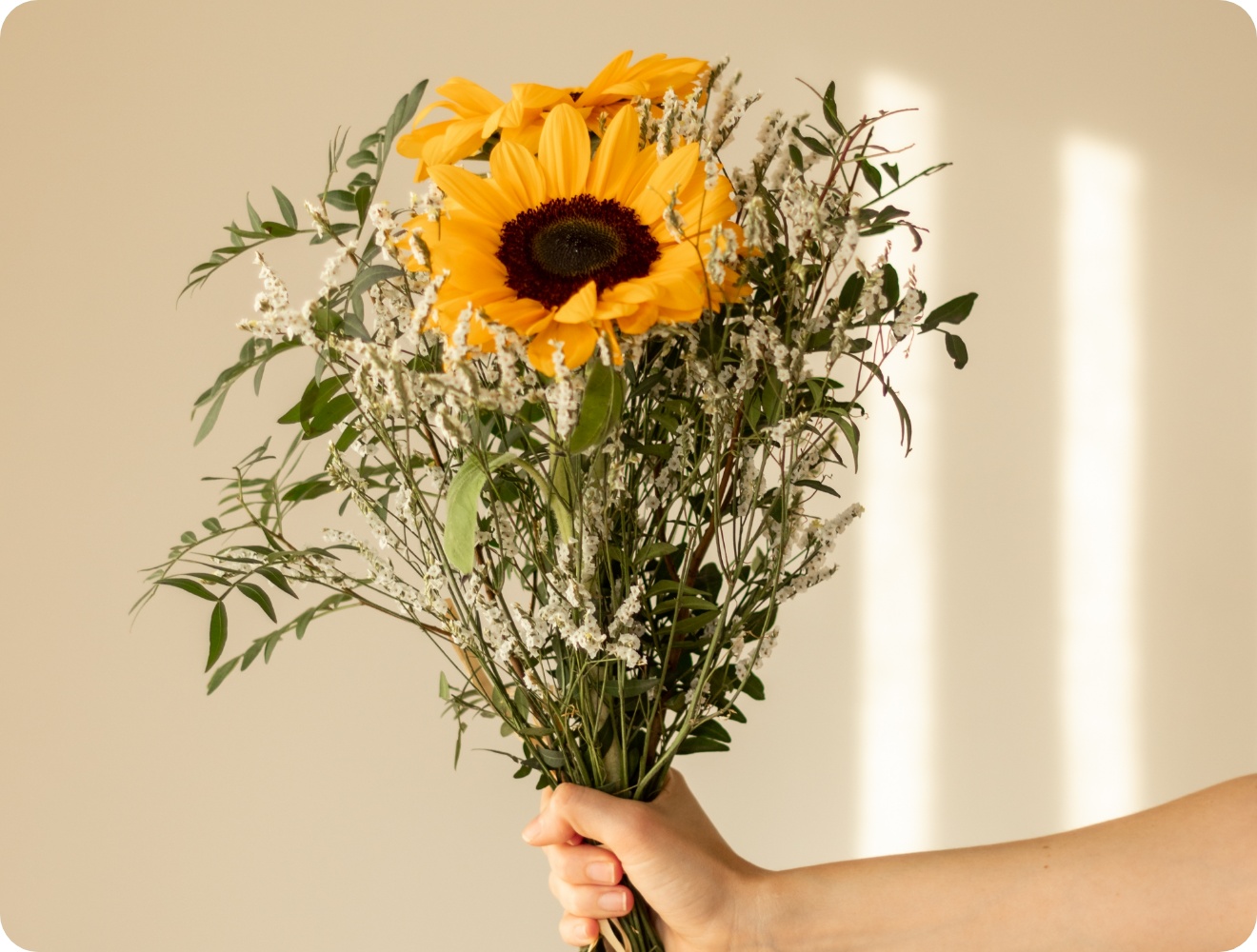 Person hält frischen Strauß mit Sonnenblumen und Grünzeug in der Hand.