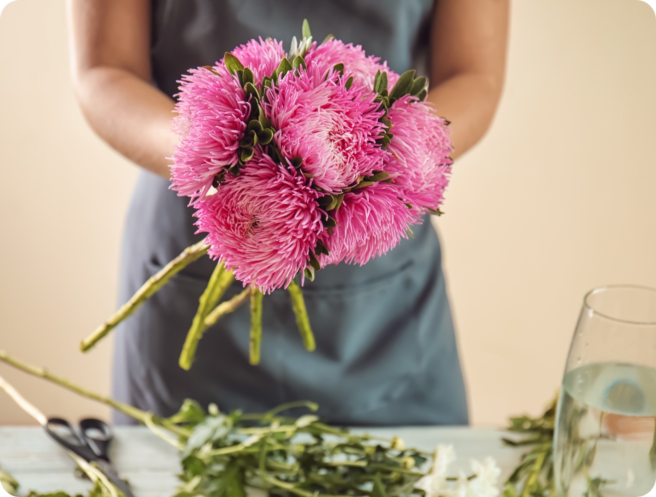 Floristin bindet Strauß aus leuchtend pinken Chrysanthemen auf rustikalem Holztisch..